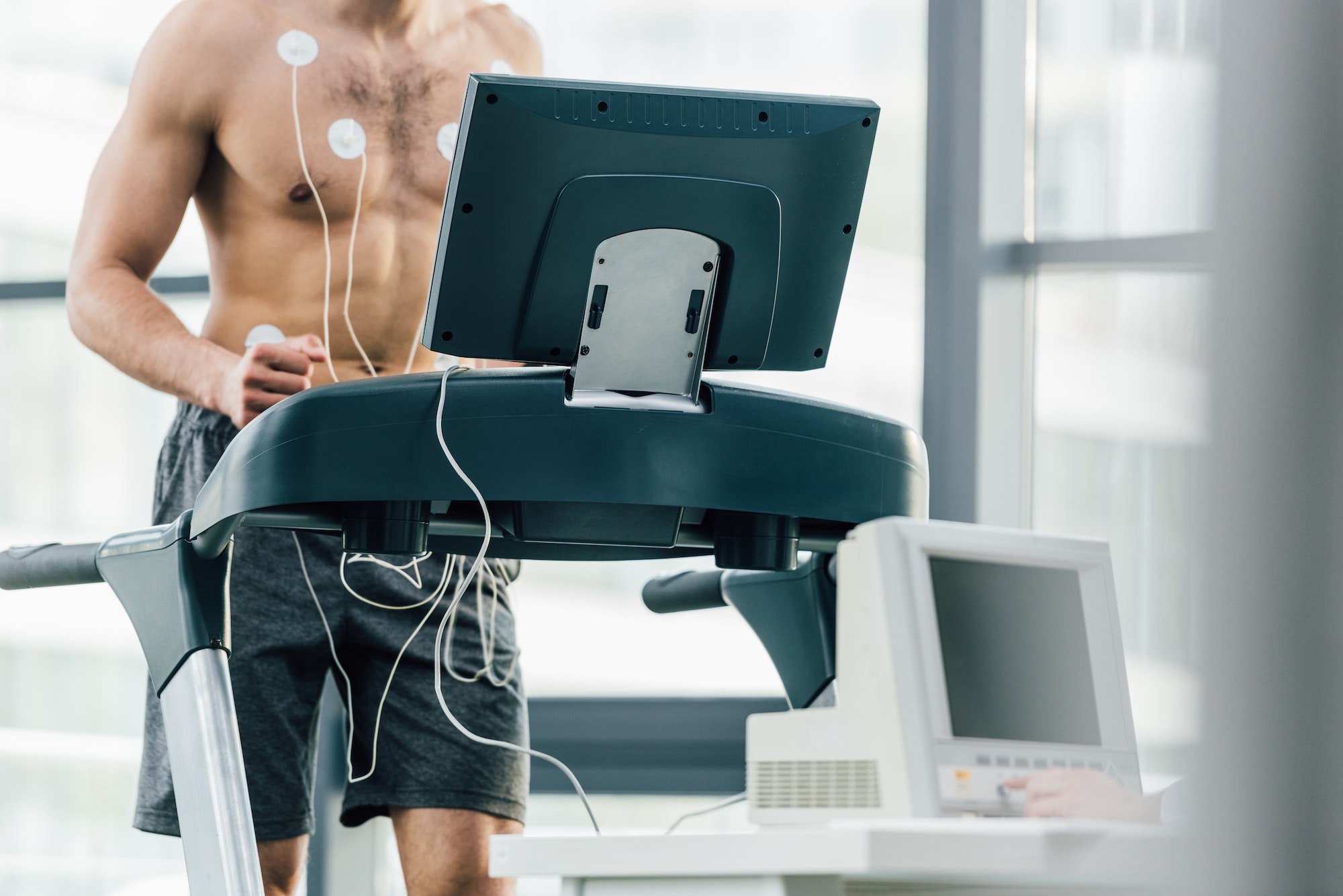 selective focus of sportsman with electrodes running on treadmill during endurance test in gym