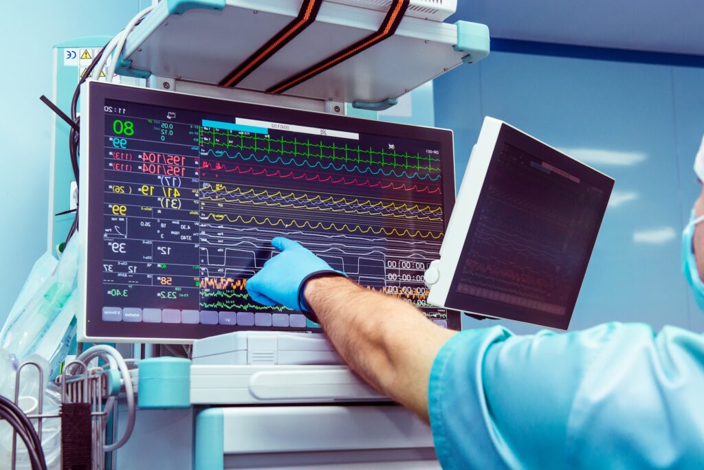 Male anaesthesiologist hand pointing vital activity data at modern monitor system in operation room